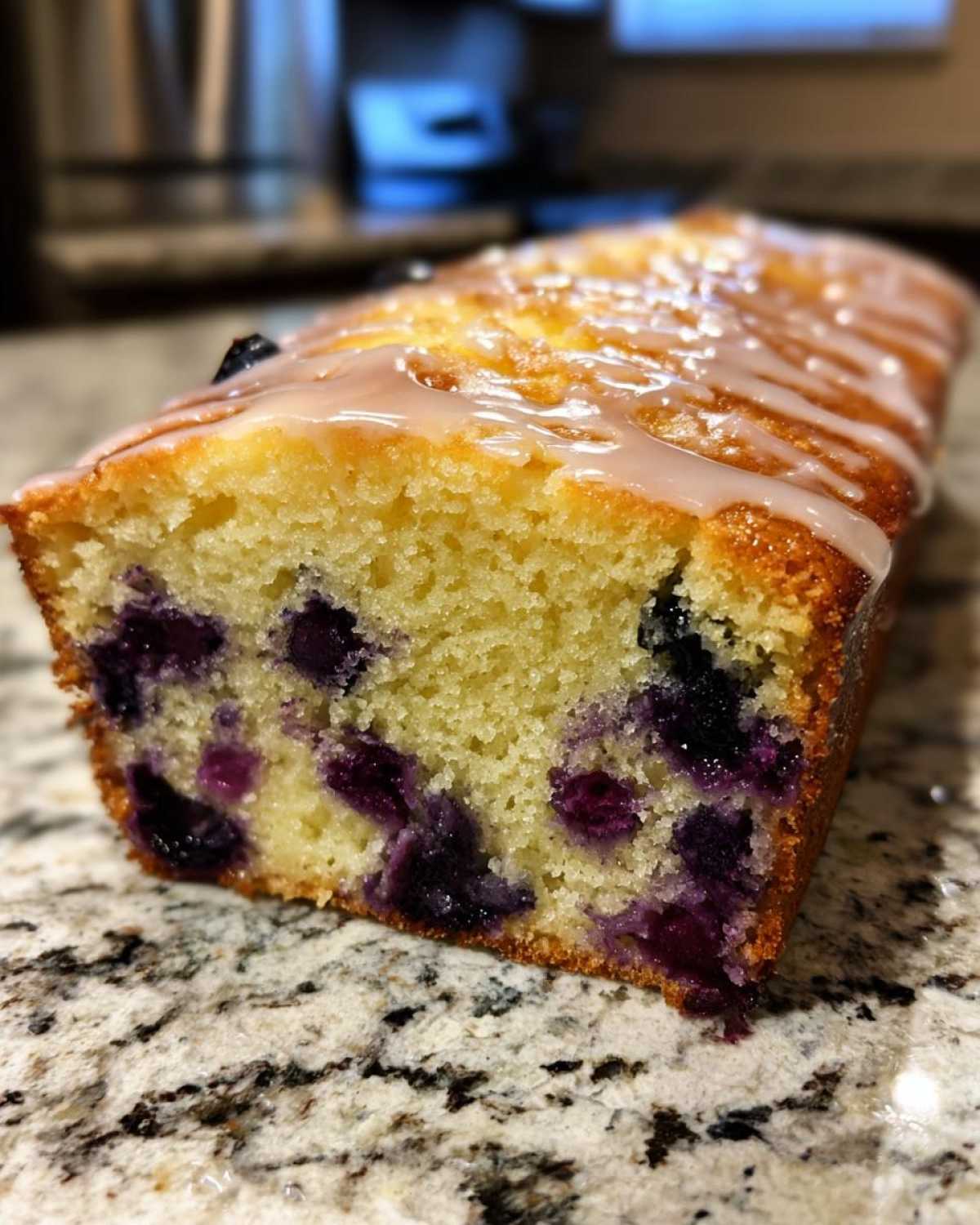 Close-up cross-section of a moist Lemon Blueberry Yogurt Loaf showing bright blueberries and a sweet lemon glaze.