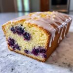 A close-up of a moist Lemon Blueberry Yogurt Loaf drizzled with a thick white glaze.
