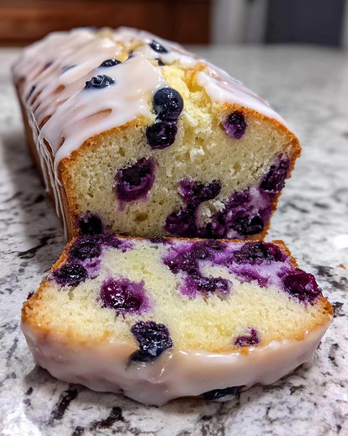 Close-up of a sliced Lemon Blueberry Yogurt Loaf showing moist crumb and generous blueberries, topped with white glaze.