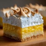 Close-up of a thick square of Lemon Meringue Pie Bars showing crust, bright yellow filling, and toasted meringue.