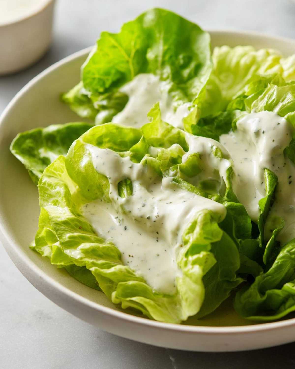 Close-up of crisp green lettuce leaves generously topped with creamy Copycat Olive Garden Salad Dressing.