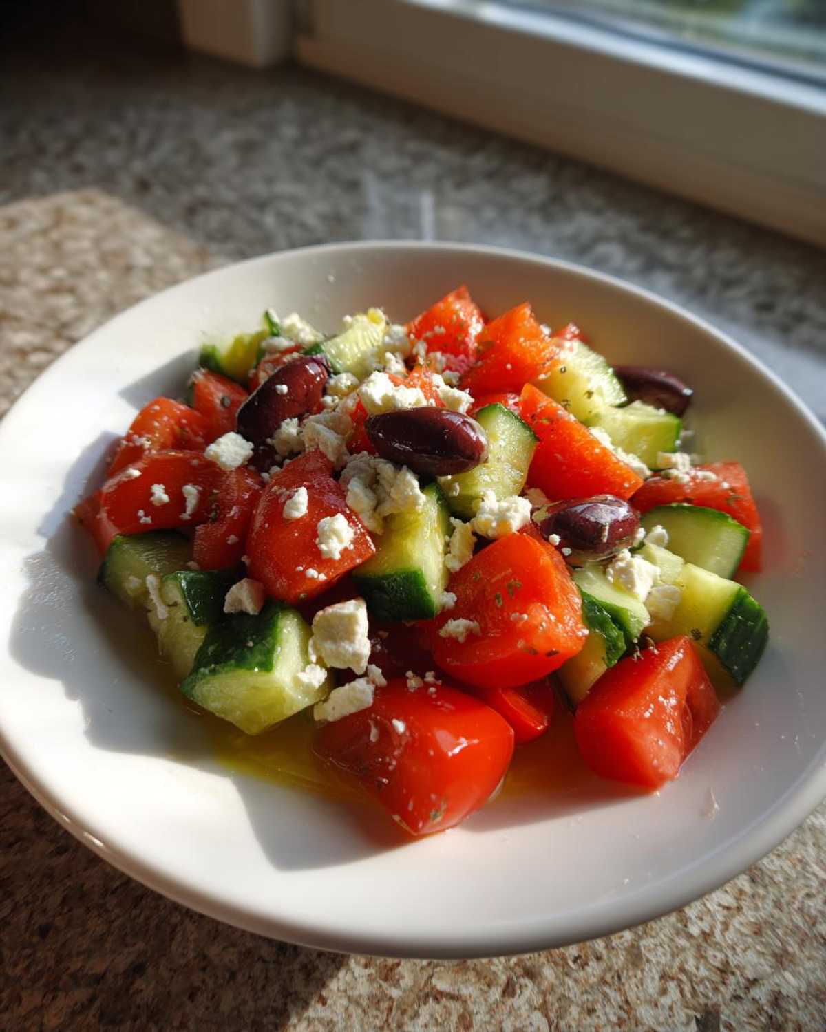 Close-up of a white bowl filled with Mediterranean Cucumber Tomato Salad, featuring chunks of tomato, cucumber, feta, and olives.