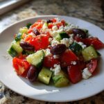 A vibrant plate of Mediterranean Cucumber Tomato Salad topped with feta cheese and Kalamata olives.