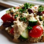 Close-up of a vibrant Mediterranean Quinoa Bowl topped with cherry tomatoes, cucumber, feta, olives, and drizzled with lemon tahini sauce.