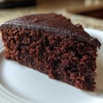 Close-up of a rich, dark slice of Gluten-Free Chocolate Cake with a thin chocolate glaze on a white plate.