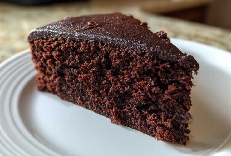 Close-up of a rich, dark slice of Gluten-Free Chocolate Cake with a thin chocolate glaze on a white plate.