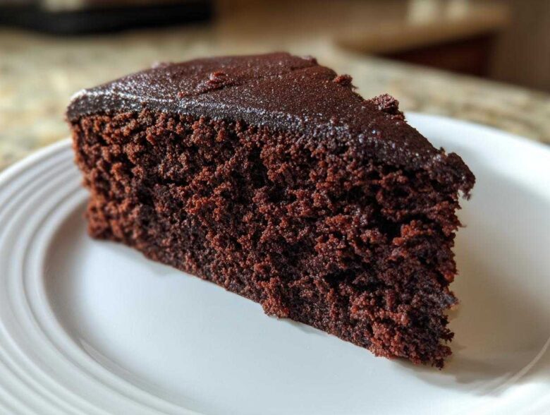 Close-up of a rich, dark slice of Gluten-Free Chocolate Cake with a thin chocolate glaze on a white plate.