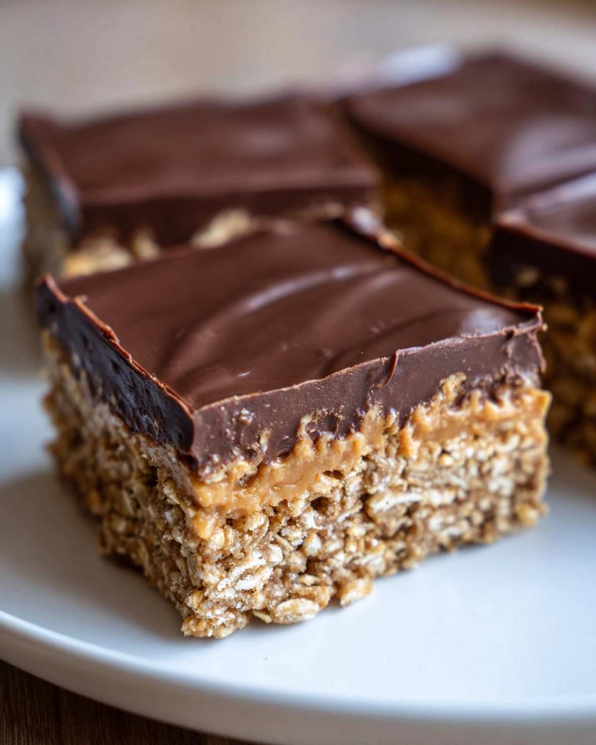 A close-up of a square of No-Bake Chocolate Peanut Butter Oat Bars showing the oat base, peanut butter layer, and chocolate topping.