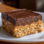 A single square of No-Bake Chocolate Peanut Butter Oat Bars showing the oat base, peanut butter layer, and chocolate topping.