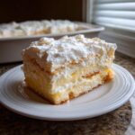 A thick slice of No-Bake Lemon Icebox Cake layered with creamy filling and topped with whipped cream on a white plate.