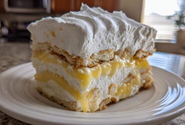 A tall slice of No-Bake Lemon Icebox Cake showing layers of lemon filling, whipped cream, and vanilla wafers.
