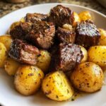 Close-up of juicy, seasoned steak bites served over golden roasted potatoes, highlighting the garlic butter sauce.
