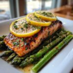 A perfectly cooked fillet of One-Pan Lemon Garlic Salmon served over bright green asparagus spears, topped with lemon slices and parsley.