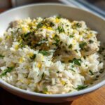 A close-up of a white bowl filled with One-Pot Chicken and Rice with Lemon and Herbs, topped with fresh parsley and lemon zest.