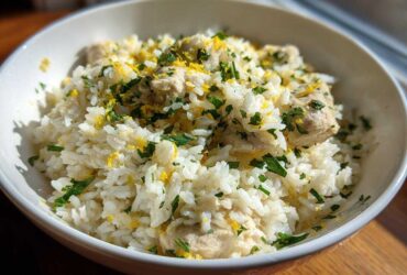 A close-up of a white bowl filled with One-Pot Chicken and Rice with Lemon and Herbs, topped with fresh parsley and lemon zest.