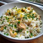 Close-up of a white bowl filled with fluffy rice, chunks of chicken, and topped with bright lemon zest and fresh parsley for One-Pot Chicken and Rice with Lemon and Herbs.