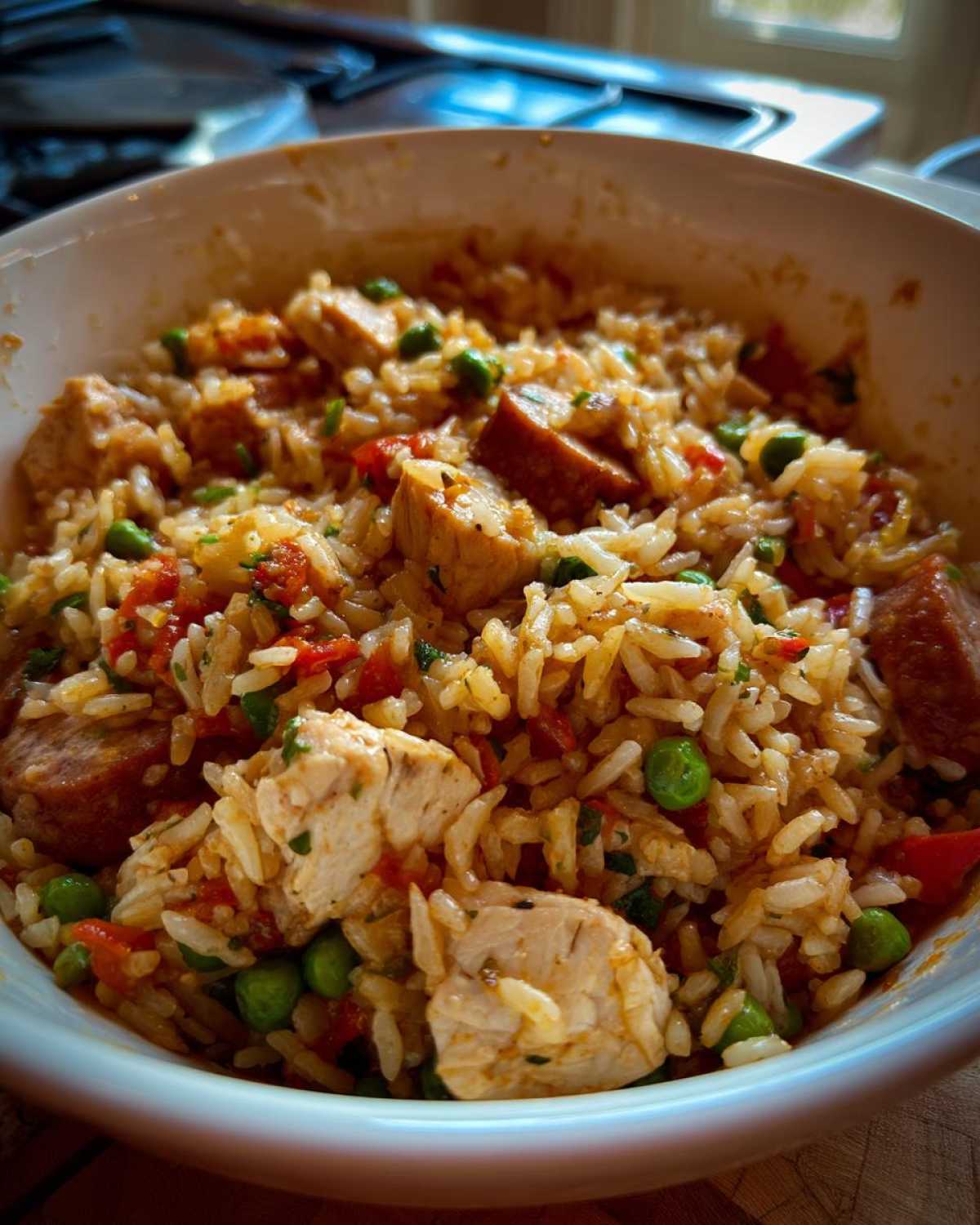 Close-up of a white bowl filled with flavorful One-Pot Chicken Jambalaya, featuring rice, chicken chunks, sausage, and green peas.
