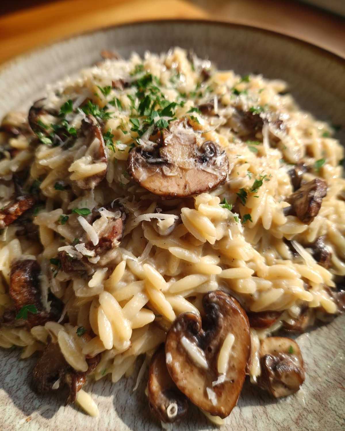 A close-up of creamy One-Pot Creamy Mushroom Orzo topped with sliced mushrooms, grated cheese, and fresh parsley.
