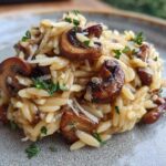 Close-up of a serving of One-Pot Creamy Mushroom Orzo, topped with sautéed mushrooms and fresh herbs.