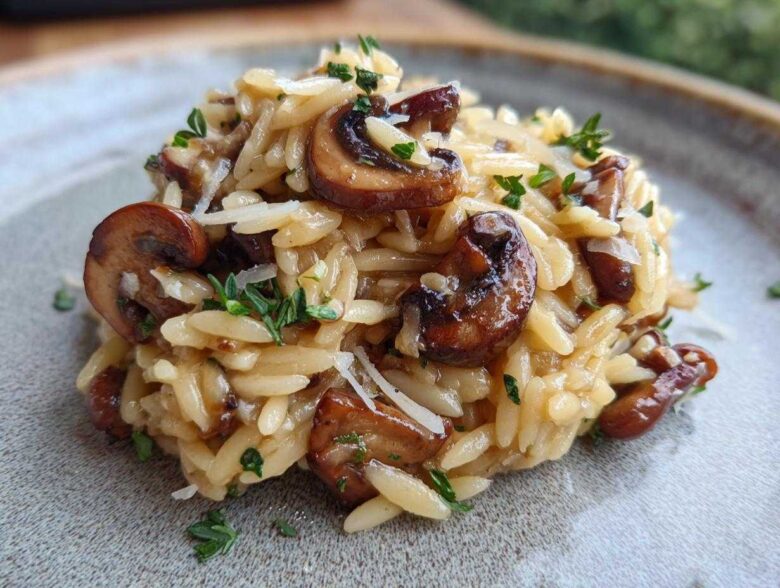 Close-up of a serving of One-Pot Creamy Mushroom Orzo, topped with sautéed mushrooms and fresh herbs.