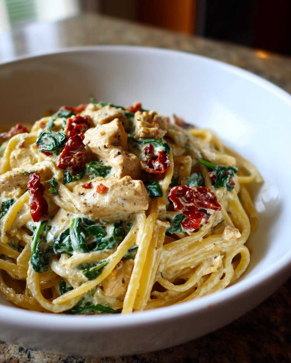Close-up of One-Pot Creamy Tuscan Chicken Pasta with spinach and sun-dried tomatoes in a white bowl.