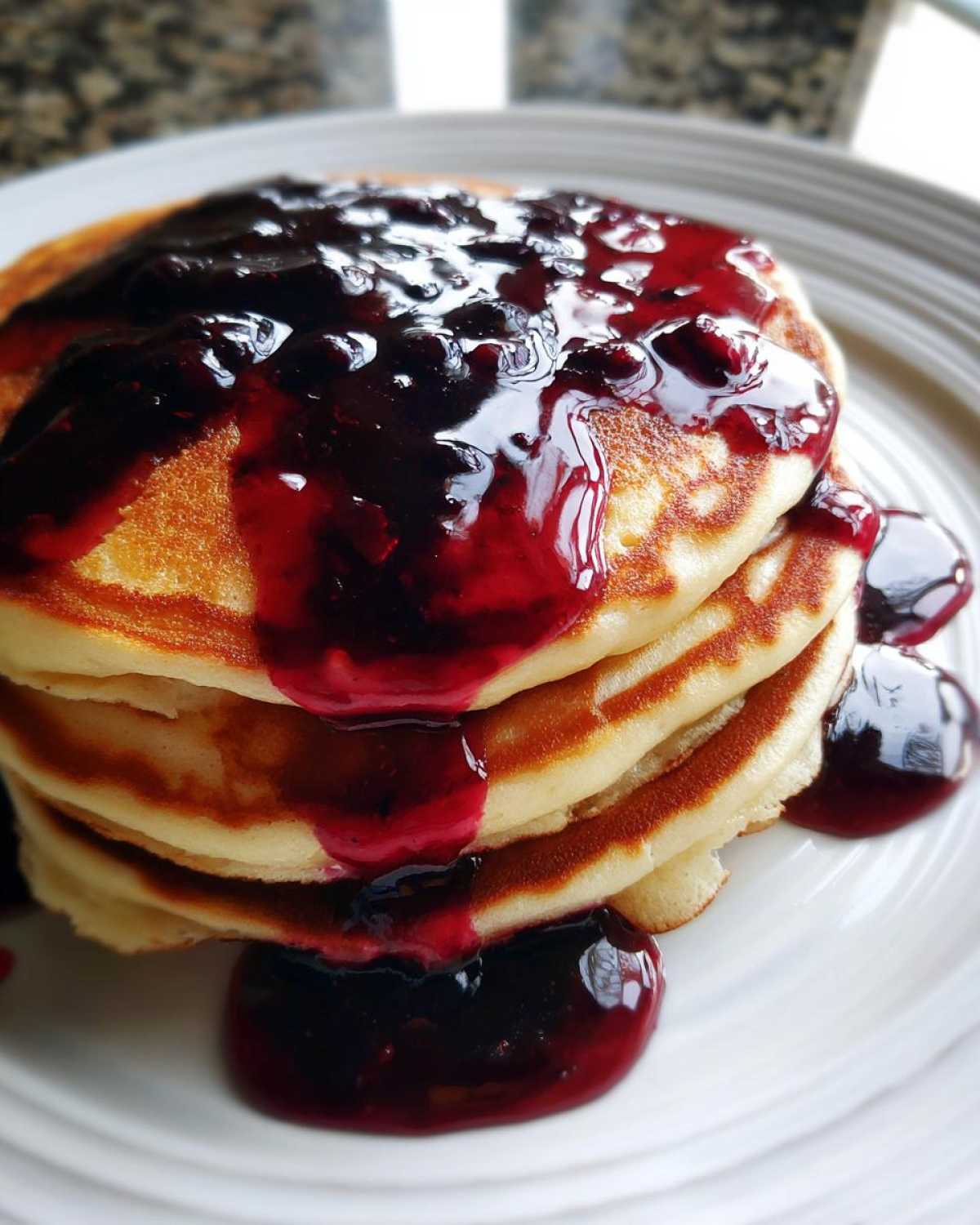 A stack of fluffy pancakes generously covered with thick, rich Homemade Blueberry Syrup.