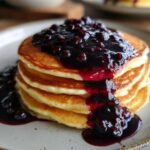 A stack of fluffy pancakes generously topped with rich Homemade Blueberry Syrup and whole berries.