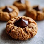 A close-up of a freshly baked Peanut Butter Blossom Cookie topped with a glossy, melted chocolate kiss.