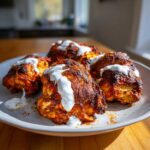Four pieces of richly spiced Sheet Pan Chicken Shawarma drizzled with white garlic yogurt sauce on a plate.