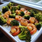Close-up of Sheet Pan Garlic Butter Shrimp and Broccoli seasoned and cooked on a metal baking sheet.