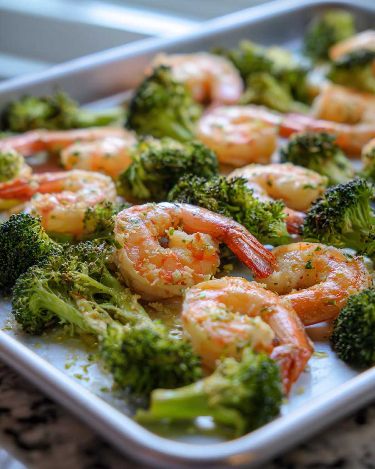 Close-up of cooked shrimp and broccoli florets coated in garlic butter on a sheet pan.