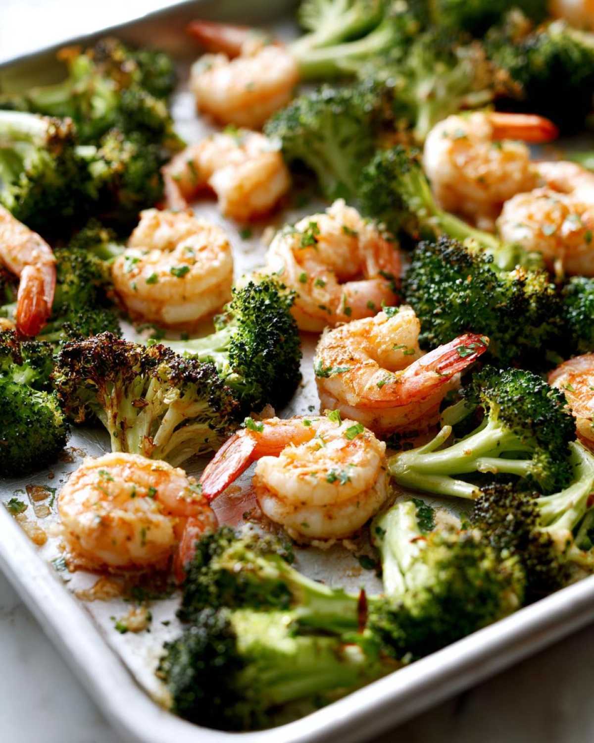 Close-up of cooked Sheet Pan Garlic Butter Shrimp and Broccoli spread across a metal baking sheet.