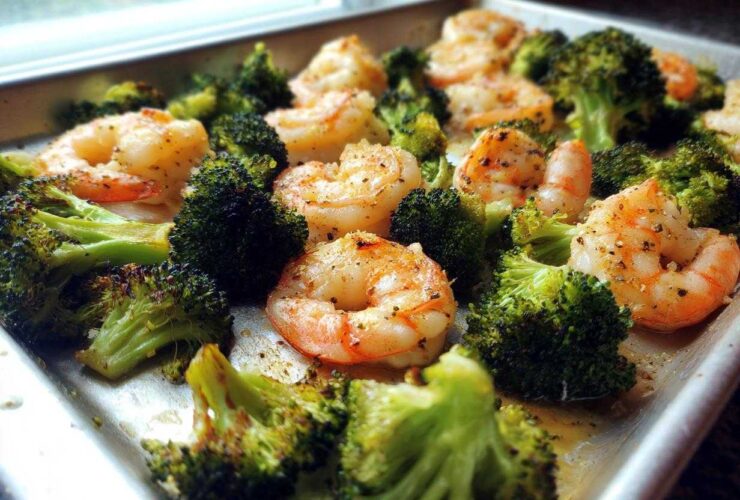 Close-up of Sheet Pan Garlic Butter Shrimp and Broccoli seasoned with pepper, glistening on a metal baking sheet.