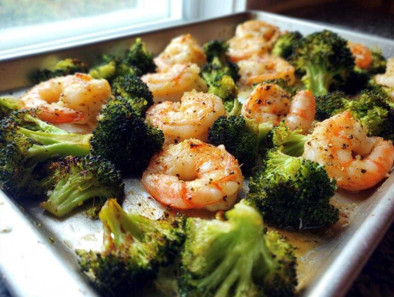 Close-up of Sheet Pan Garlic Butter Shrimp and Broccoli seasoned with pepper, glistening on a metal baking sheet.