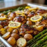 Close-up of Sheet Pan Lemon Pepper Chicken and Potatoes with roasted asparagus and lemon slices.
