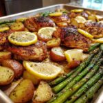 A full sheet pan of Sheet Pan Lemon Pepper Chicken and Potatoes with asparagus and lemon slices.