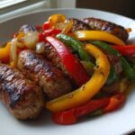 Close-up of browned sausages served with colorful roasted peppers and onions from Sheet Pan Sausage and Peppers.