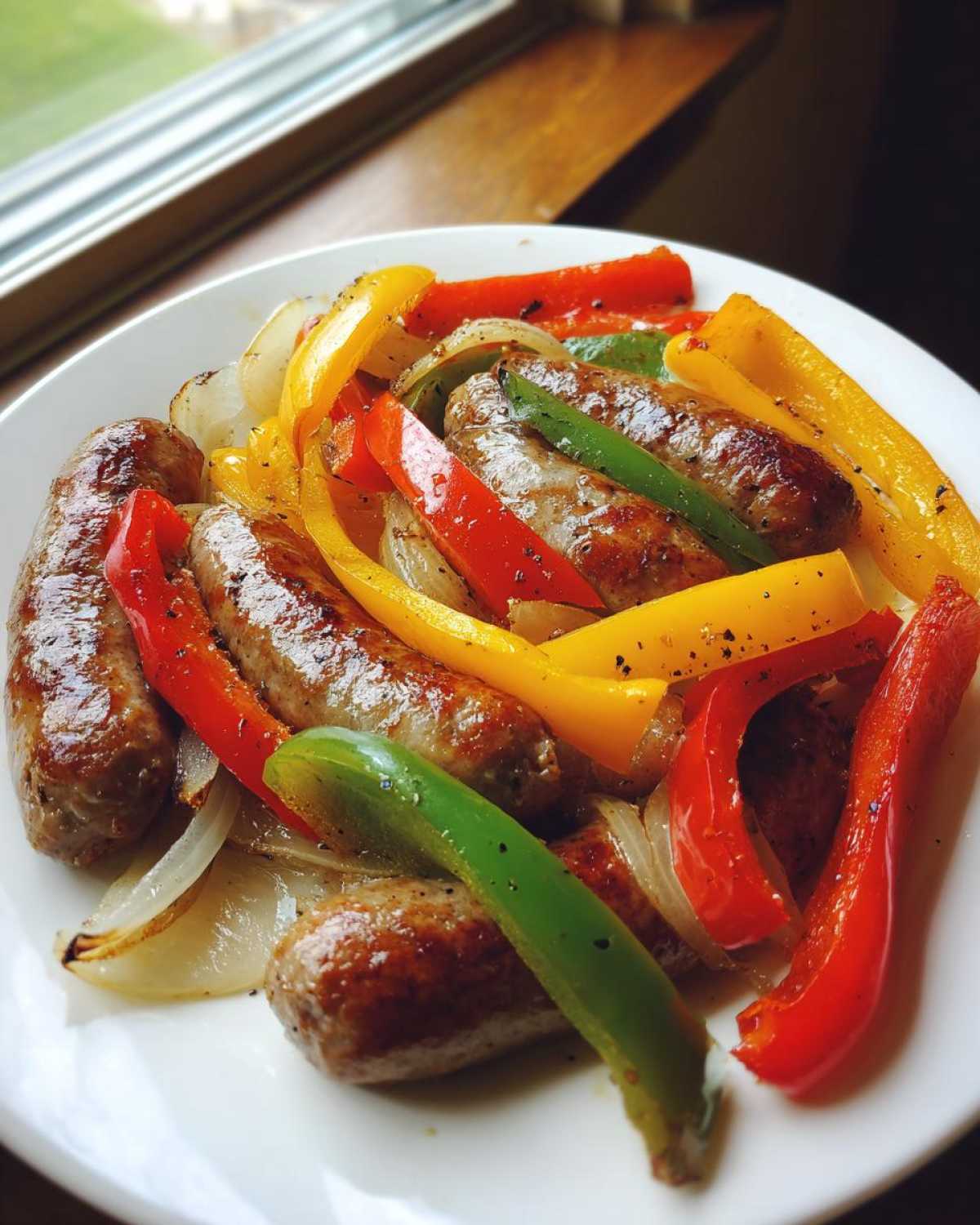 Close-up of grilled Sheet Pan Sausage and Peppers with colorful bell peppers and onions served on a white plate.