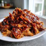 A mound of shredded Slow Cooker Honey Garlic Pulled Pork covered in a thick, glossy sauce on a white plate.