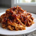 A mound of shredded, saucy Slow Cooker Honey Garlic Pulled Pork served on a white plate.