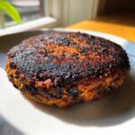 Close-up of a richly browned and slightly charred Smoky Black Bean Burger Patty on a white plate.