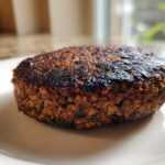 Close-up of a perfectly seared, dark brown Smoky Black Bean Burger Patty resting on a light plate.