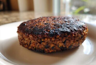 Close-up of a perfectly seared, dark brown Smoky Black Bean Burger Patty resting on a light plate.