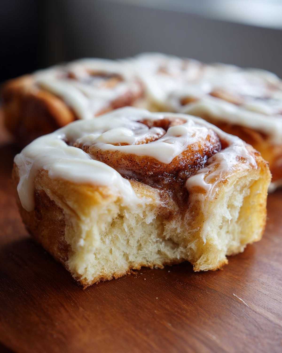 Close-up of a soft Gluten-Free Cinnamon Roll with a bite taken out, showing fluffy interior and thick white icing.