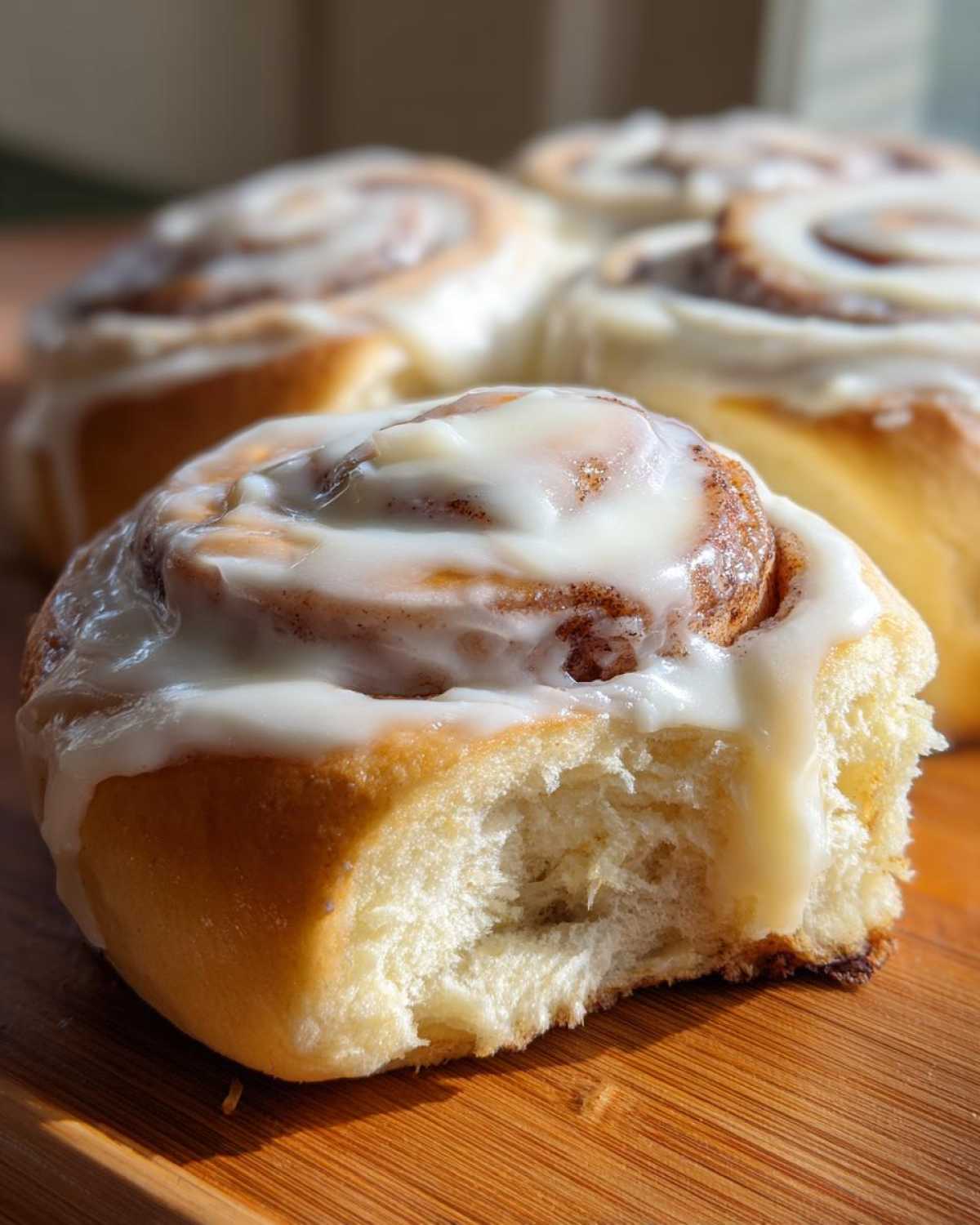 Close-up of a soft Gluten-Free Cinnamon Roll with a bite taken out, covered in white icing.