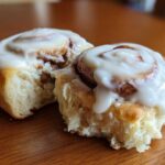 Close-up of two soft Gluten-Free Cinnamon Rolls, one broken open to show the fluffy interior and thick white frosting.
