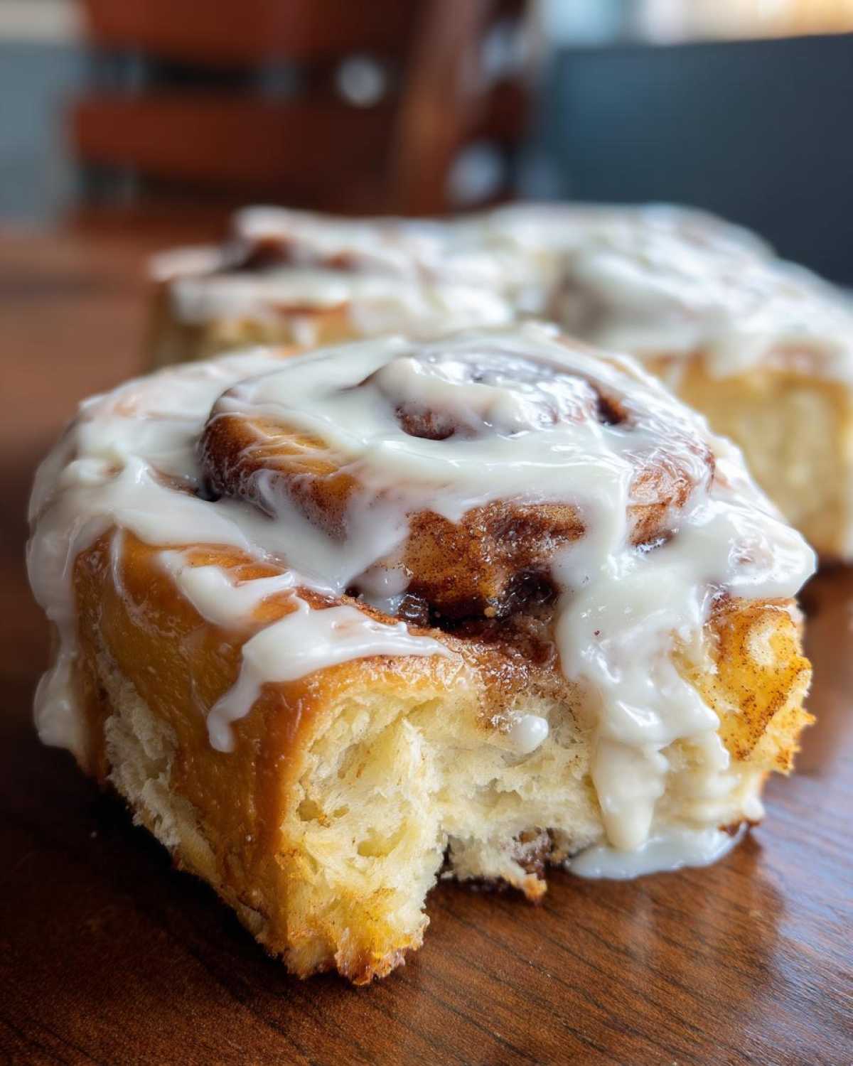 A close-up of a soft, freshly baked Gluten-Free Cinnamon Roll with thick white icing, sitting on a wooden table.