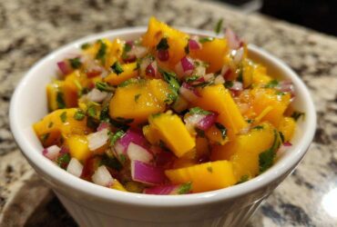 Close-up of vibrant Spicy Mango Salsa featuring chunks of yellow mango, red onion, and cilantro in a white bowl.