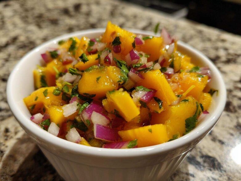 Close-up of vibrant Spicy Mango Salsa featuring chunks of yellow mango, red onion, and cilantro in a white bowl.