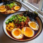 Close-up of a bowl of Spicy Miso Ramen with soft-boiled eggs, ground meat, corn, and scallions.